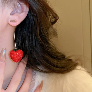 Détail de boucles d'oreilles fraises rouges avec pompons dorés portées par un mannequin