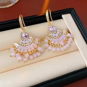 Détail de boucles d'oreilles éventail dorées avec zircon rose, perles et glands