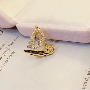 Macro view of gold sailboat brooch with white crystals and nautical wheel detail