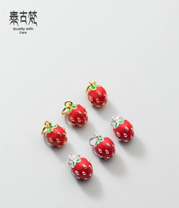 Macro view of strawberry pendants with red enamel finish and gold or silver accents