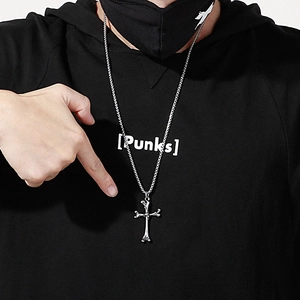 Close-up of a silver cross bone pendant on a box chain worn by a model in streetwear
