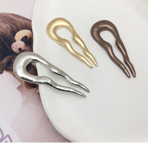 Three minimalist metal U-shaped hair pins in gold, silver, and bronze on ceramic plate