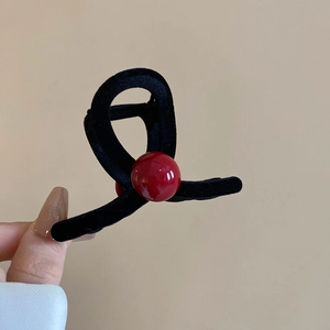 Detail of black flocked shark hair clip with a red bead on beige background