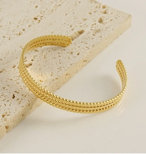 Close-up of vintage gold wheat pattern bangle on beige stone surface with soft lighting