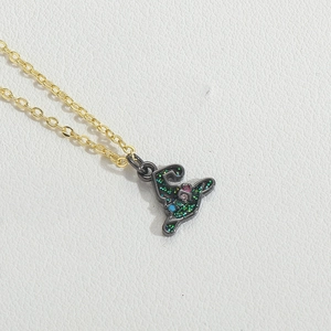 Close-up of a vintage witch hat pendant with green glitter and rhinestones on a gold chain