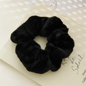 Close-up of a soft black plush rabbit fur scrunchie on a vintage calligraphy background
