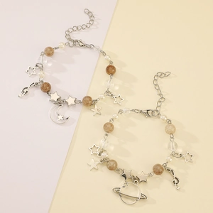 Detail of silver star bracelets with moon and Saturn charms on a pastel split background
