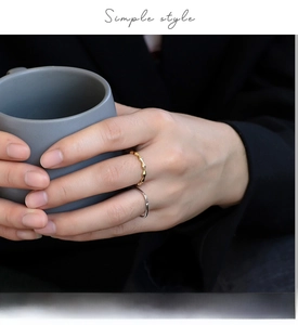 Detailed shot of gold bamboo style ring and slim silver band on hand with a cup