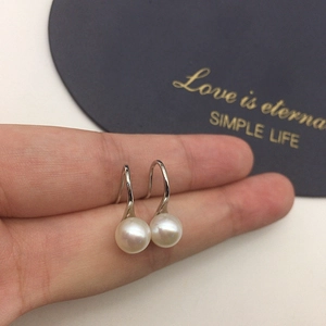 Macro view of high-luster freshwater pearl drop earrings on silver hooks with card