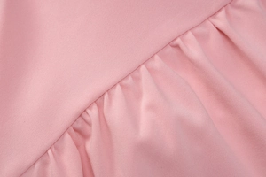 Detailed macro view of pink woven fabric showing ruffle textures and soft light reflections