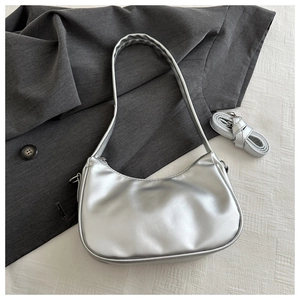 Silver metallic crescent underarm bag with detachable strap on textured fabric background