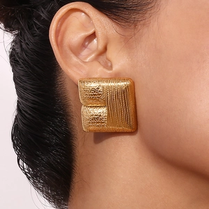Close-up of golden square earrings with hammered and vertical stripe texture on a model