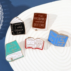 Set of five colorful enamel book brooches with creative lettering on a white display tray