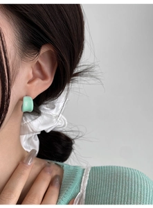 Close-up of mint green resin C-shape earring worn on ear with soft lighting