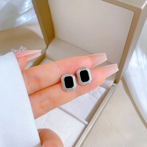 Macro shot of silver square stud earrings with black rectangular surface on fingers