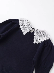 Detail of dark knit sweater featuring a contrasting white lace collar and button closure