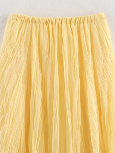 Detail view of yellow pleated fabric texture and elastic waistband of the maxi skirt