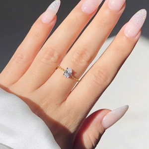 Detail view of a gold-plated chain ring with an oval clear zircon stone on a finger