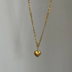 Detailed view of 3D gold heart pendant on a polished Figaro chain necklace