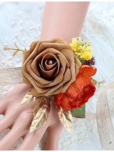 Detail of handmade bridal wrist corsage with silk roses and gold leaves on lace background
