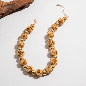 Détail du collier avec pompons léopard et perles dorées polies sur fond blanc neutre
