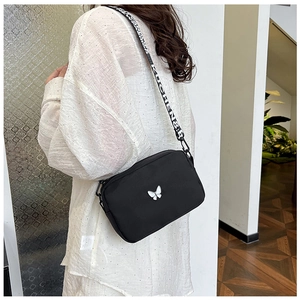 Detail of nylon crossbody bag featuring white butterfly print and wide lettered strap