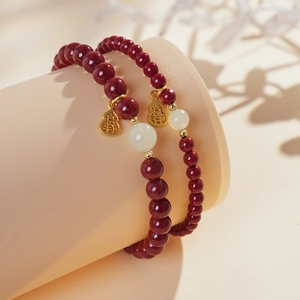 Macro detail of cinnabar beads and golden gourd charms with jade accents on bracelet