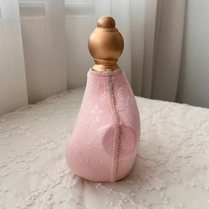 Pink vintage perfume bottle with floral fabric texture and golden spherical cap detail
