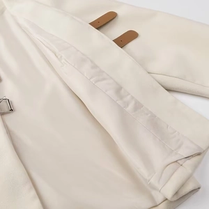 Detail of off-white wool coat featuring brown leather buckle straps and soft texture