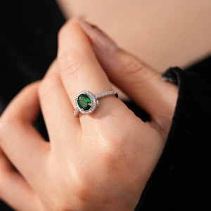 Macro shot of silver halo ring with oval green zircon and pavé setting on finger