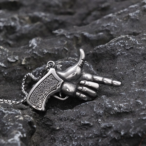 Macro detail of retro silver pistol gesture pendant on dark rugged stone background
