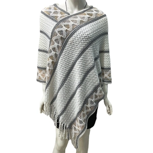 Detail shot of white knitted poncho featuring gray stripes and brown ethnic patterns with tassels
