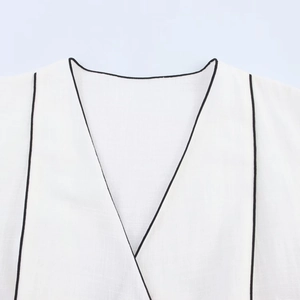 Detailed close-up of a white V-neck top with contrasting black piping and woven fabric texture