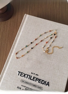 Close-up of a colorful beaded necklace on a textile book with a gold lobster clasp