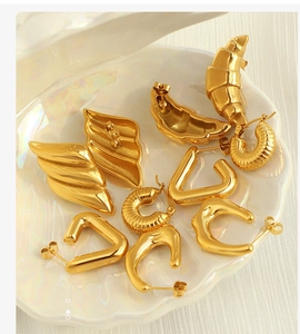 Close-up of 18k gold croissant earrings and geometric textured studs in a shell bowl