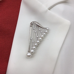 Detail of silver harp brooch with white pearls and crystals on a white blazer