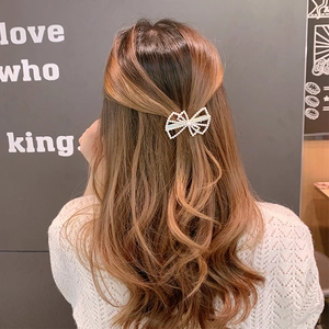 Detail view of a white pearl bow hair clip worn by a model with wavy brown hair