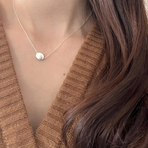Close-up of a minimalist 925 silver bean pendant necklace worn over a brown sweater