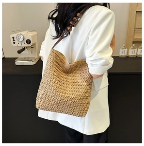 Detail of hand-woven straw bag featuring wooden bead shoulder strap on a white blazer
