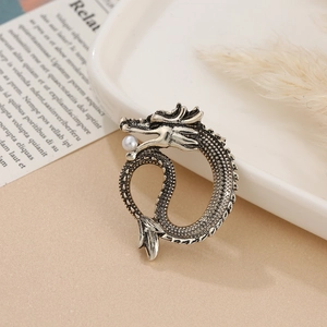 Macro shot of silver dragon brooch featuring detailed scales and a small pearl accent