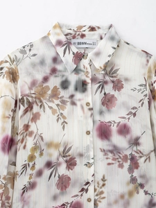 Dettaglio di camicia in chiffon bianco con fiori e strisce dorate sul colletto
