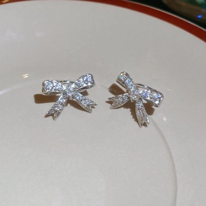 Dettaglio di orecchini a fiocco in argento con zirconi scintillanti su piatto bianco
