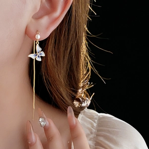 Close-up of long gold butterfly tassel earrings with pearls on a model in profile