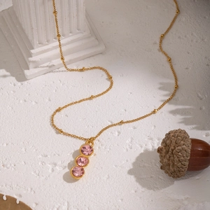 Detail of gold Y-necklace with three round pink gemstones on a white textured surface
