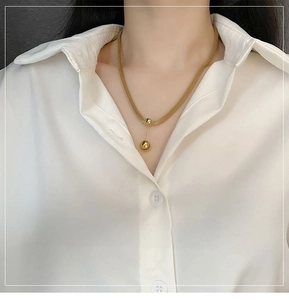 Dettaglio di una collana con ciondolo a sfere dorate su catena intrecciata su modella