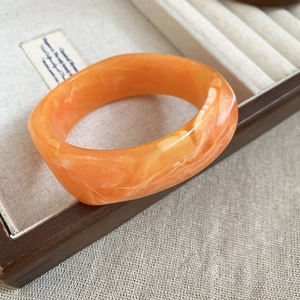 Close-up of thick resin bangle featuring orange and white marble textures on linen
