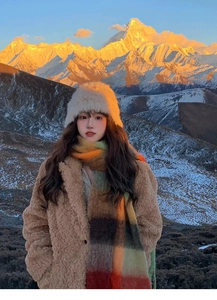 Close-up of a plaid rainbow scarf and teddy coat against a sunset snowy mountain peak