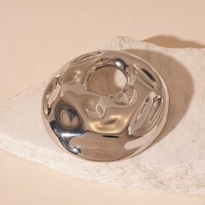 Detailed macro view of a silver circular brooch with irregular fluid metal ripple textures