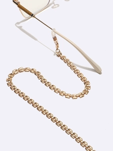 Flat link gold metal glasses chain attached to frame temple on reflective white surface