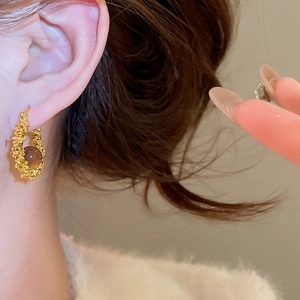 Close-up of golden resin hoop earrings with brown gemstone on model for autumn style